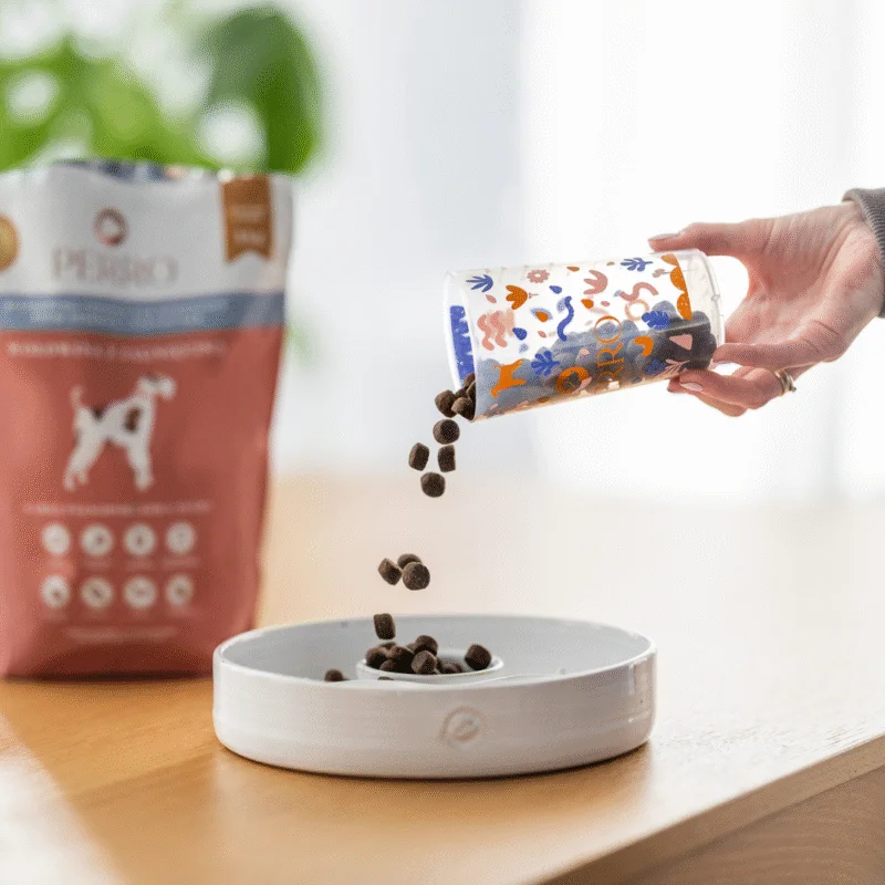 dłon nasypuąca karmę z miarki do psiej miski