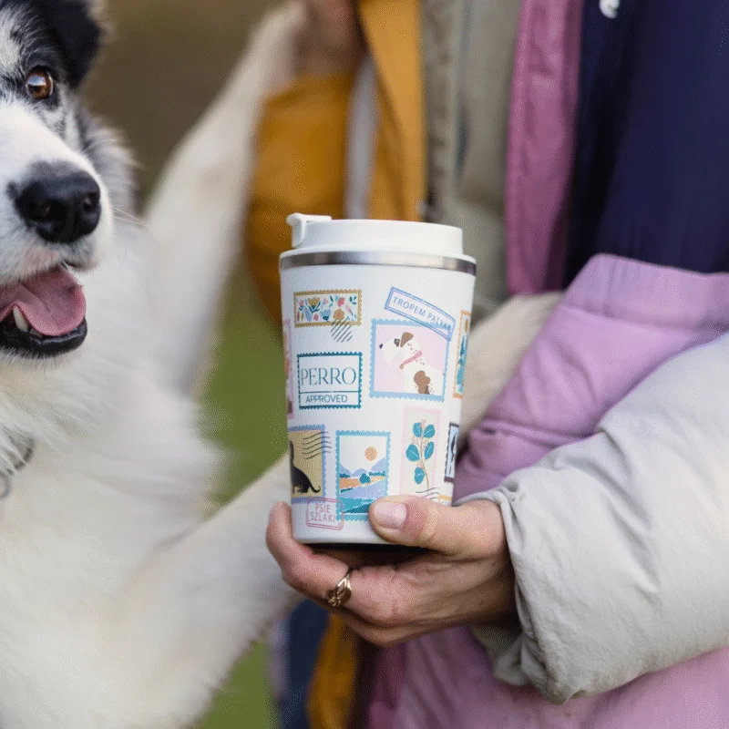 pies wdrapujący się na kobietę trzymającą kubek termiczny